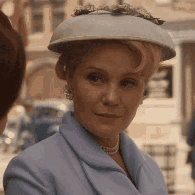 a woman wearing a hat and pearls looks to the side