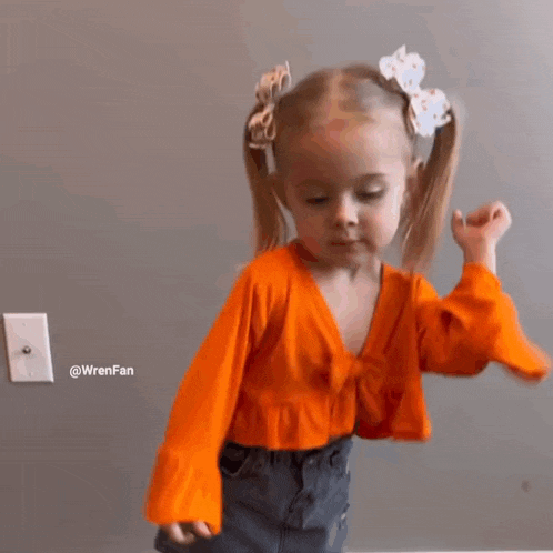 a little girl wearing an orange crop top and denim shorts is dancing in a room .