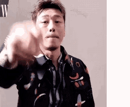 a man is pointing his finger at the camera while wearing a floral shirt .