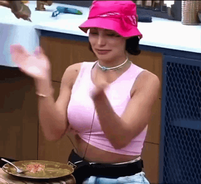 a woman wearing a pink hat and a pink crop top is sitting at a table with a plate of food .