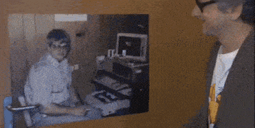 a man in a plaid shirt is sitting in front of a screen