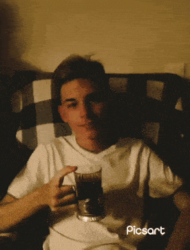 a young man is sitting in a chair holding a cup of coffee and the word picsart is on the bottom right