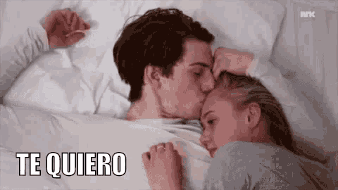 a man is kissing a woman on the forehead while they are laying in bed .