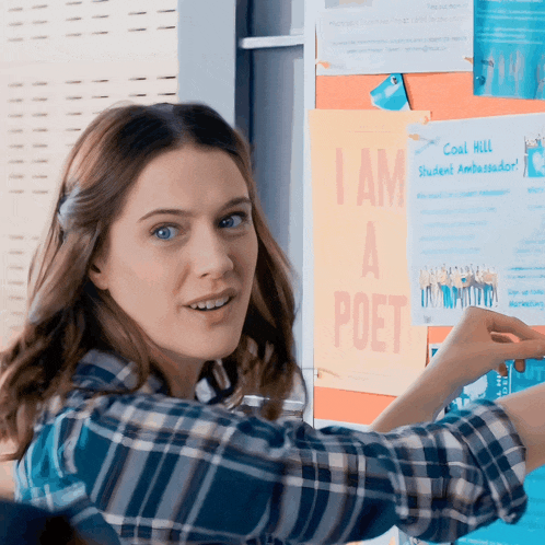 a woman in a plaid shirt points to a poster that says i am a poet