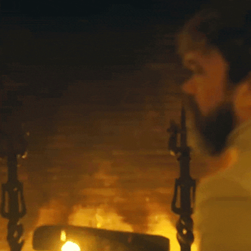 a man with a beard is standing in front of a fireplace in a dark room .
