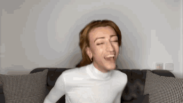 a woman is sitting on a couch making a funny face and laughing .