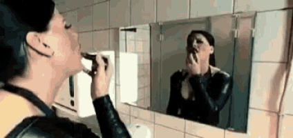 a woman is applying lipstick in front of a mirror in a public restroom .