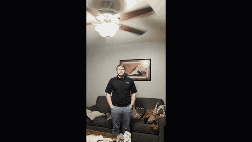 a man standing in a living room with a ceiling fan behind him