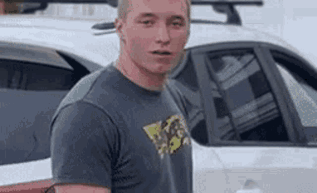 a man in a grey shirt is standing in front of a car .