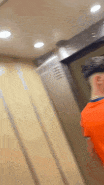 a man is standing in an elevator wearing an orange shirt .