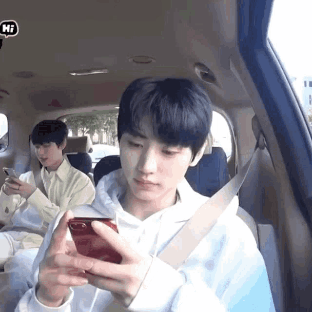 a young man is sitting in the back seat of a car looking at his cell phone .