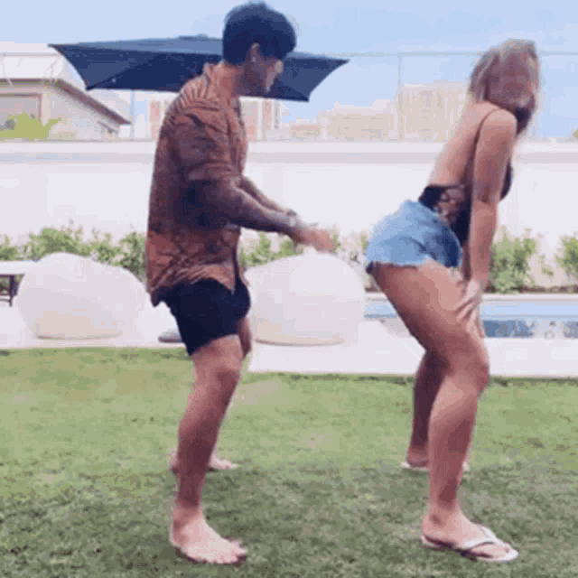 a man and a woman are dancing in the grass in front of a swimming pool .