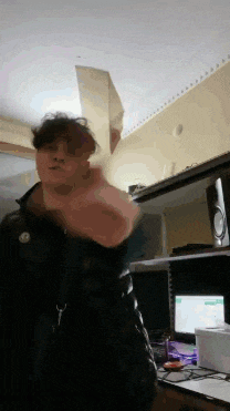 a man in a black jacket is standing in front of a computer desk holding a piece of paper in his hand .