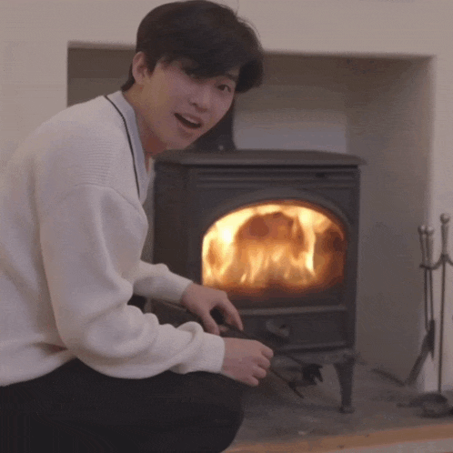 a man in a white sweater is kneeling in front of a fireplace with flames coming out of it