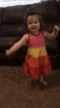 a little girl in a colorful dress is dancing in front of a couch