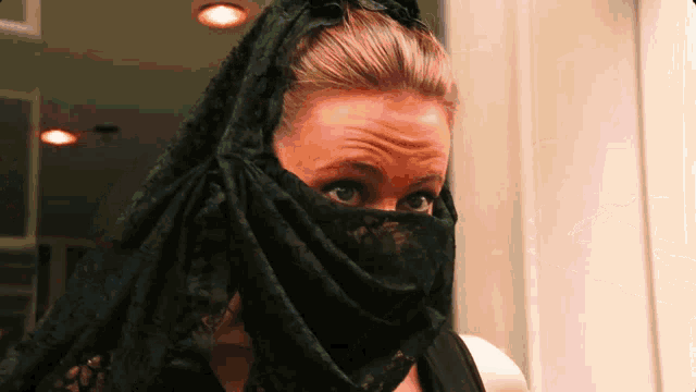 a woman wearing a black scarf covering her face looks at the camera