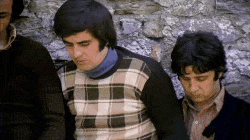 a man in a plaid sweater sits next to two other men