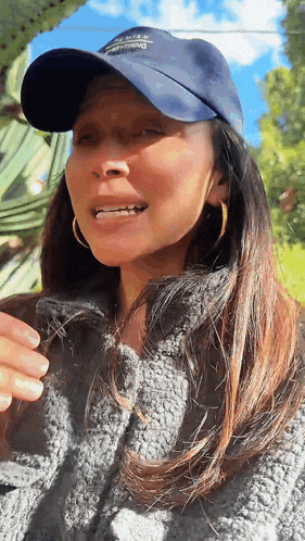a woman wearing a hat and a sweater is standing in front of a tree .