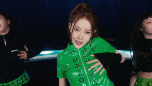 a group of women are dancing in a dark room and one of them is wearing a green shirt