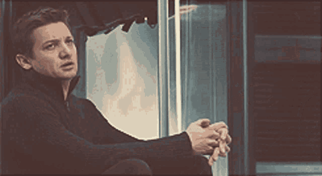 a man in a black sweater looks out a window