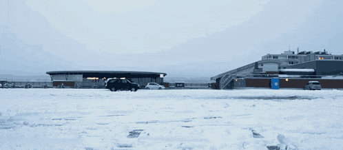 a car is parked in a snowy parking lot with a building in the background