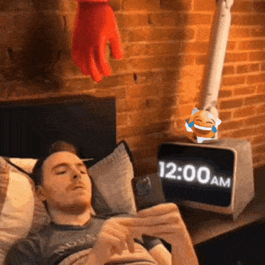 a man laying in bed looking at his phone with a clock that says 12:00 am