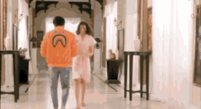 a man in an orange jacket with a smiley face on the back is walking with a woman