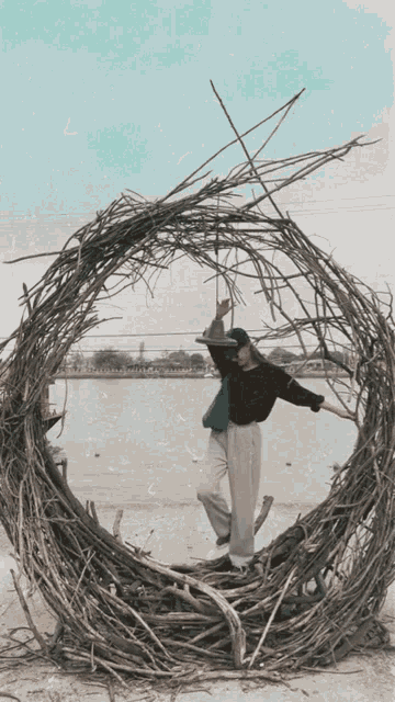 a woman stands in a circle of branches on a beach