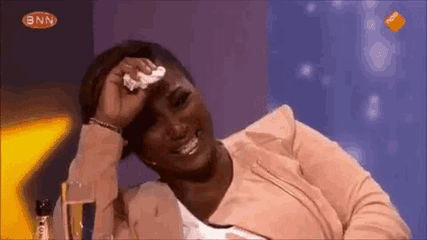 a woman is sitting at a table with a glass of champagne and wipes her forehead with a napkin .