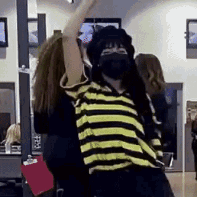 a woman wearing a mask and a striped shirt is dancing in a room with other people .