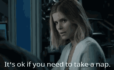 a woman is sitting at a desk with the words `` it 's ok if you need to take a nap '' written above her .