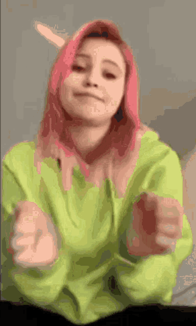 a girl with pink hair is wearing a green sweater and making a funny face .