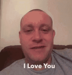 a man in a blue shirt is sitting on a couch and saying `` i love you '' .