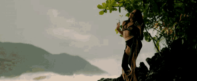 a woman in a bikini stands on a rock near a tree