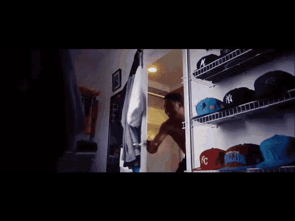 a shirtless man stands in front of a closet full of hats including one that says ny