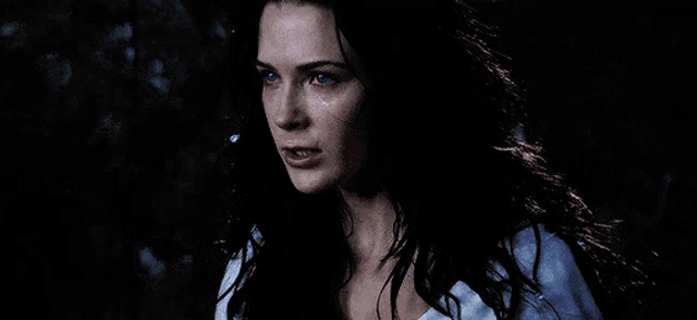 a woman with long black hair and blue eyes is looking at the camera .