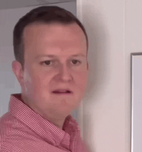 a man in a red and white checkered shirt is making a funny face while standing next to a door .