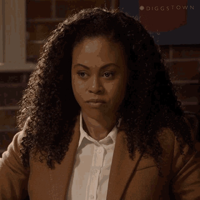 a woman with curly hair is wearing a brown jacket and a white shirt