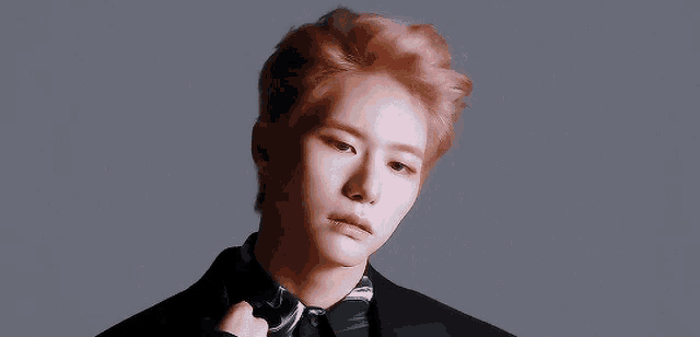 a young man with pink hair is wearing a black suit and striped shirt .