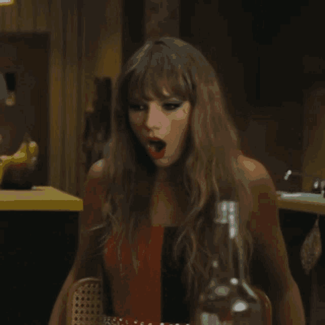 a woman is sitting at a table with her mouth open and a bottle of wine .