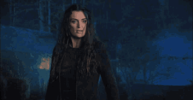 a woman with long hair is standing in a dark forest at night .
