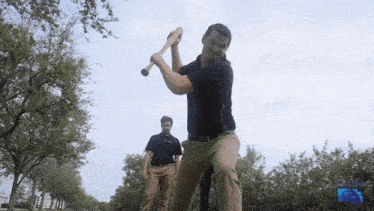 a man is swinging a baseball bat while another man watches in the background