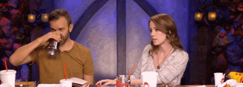 a man and a woman are sitting at a table drinking soda and eating food .