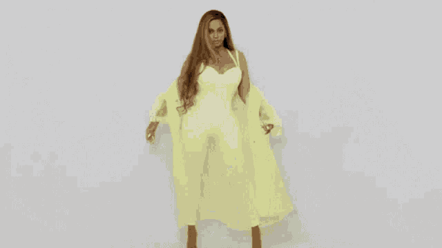 a woman in a yellow dress is standing in front of a white wall .