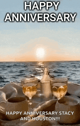 a happy anniversary greeting card with two glasses of wine on a table by the ocean .