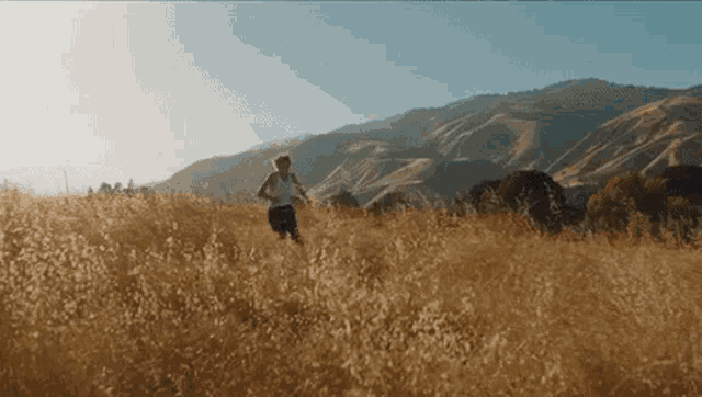 a person is running through a field of tall grass with mountains in the background