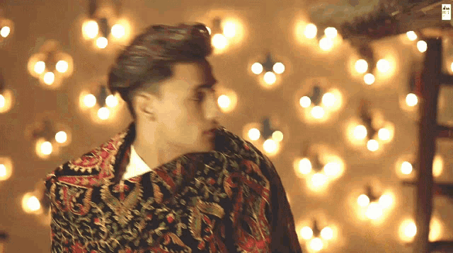 a man in a colorful jacket stands in front of a wall of lights and a sign that says ' a ' on it