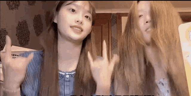two girls with long hair are standing next to each other and waving their hands .