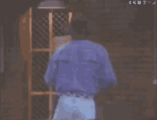 a man wearing a cowboy hat and blue shirt is dancing in front of a brick wall .