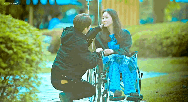 a man is kneeling down next to a woman in a wheelchair with an iv in her hand .